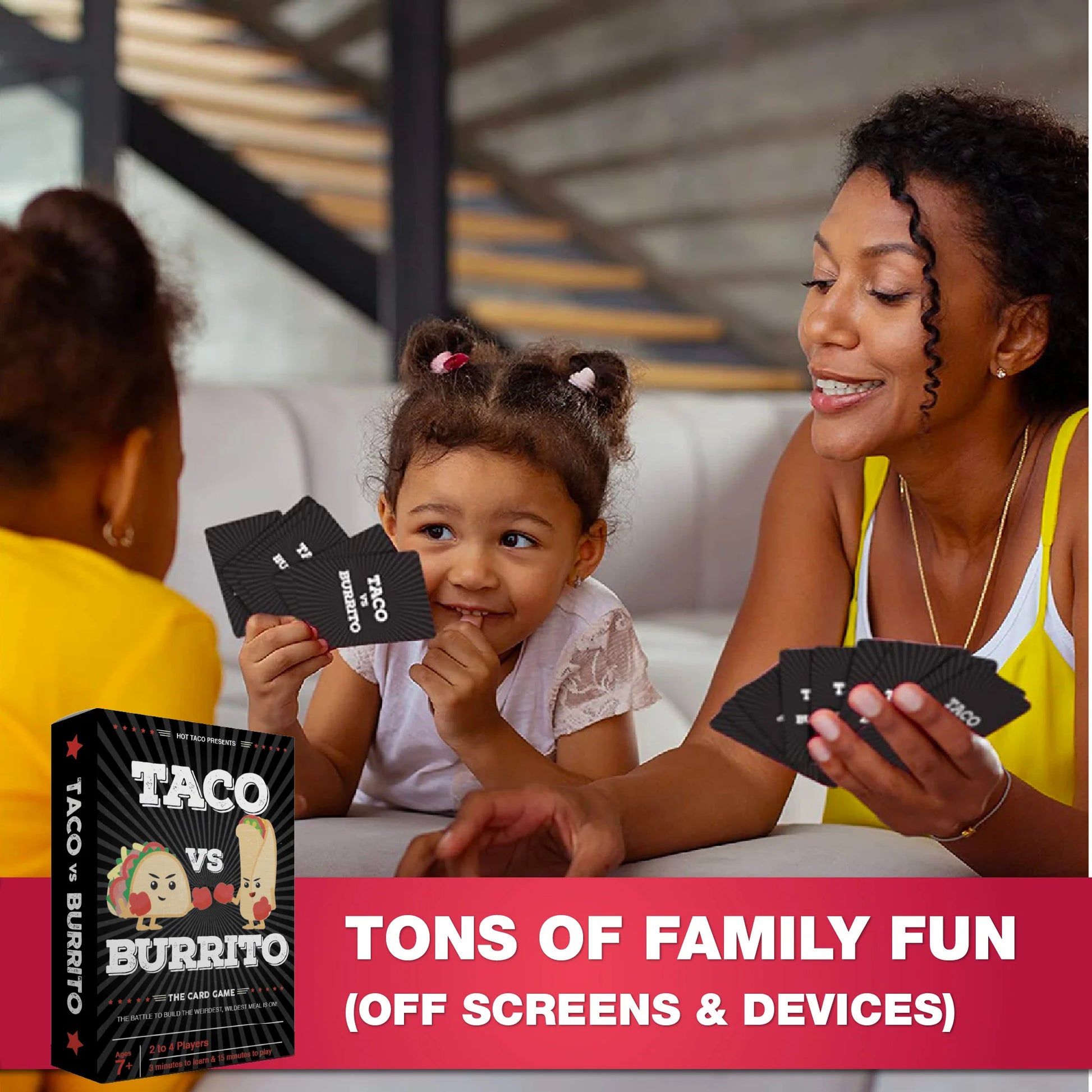 A woman and a young girl are sitting on a couch playing a card game, with the product box and cards shown in the foreground. The box is labeled 'TACO vs BURRITO' and the cards are black with white text.
