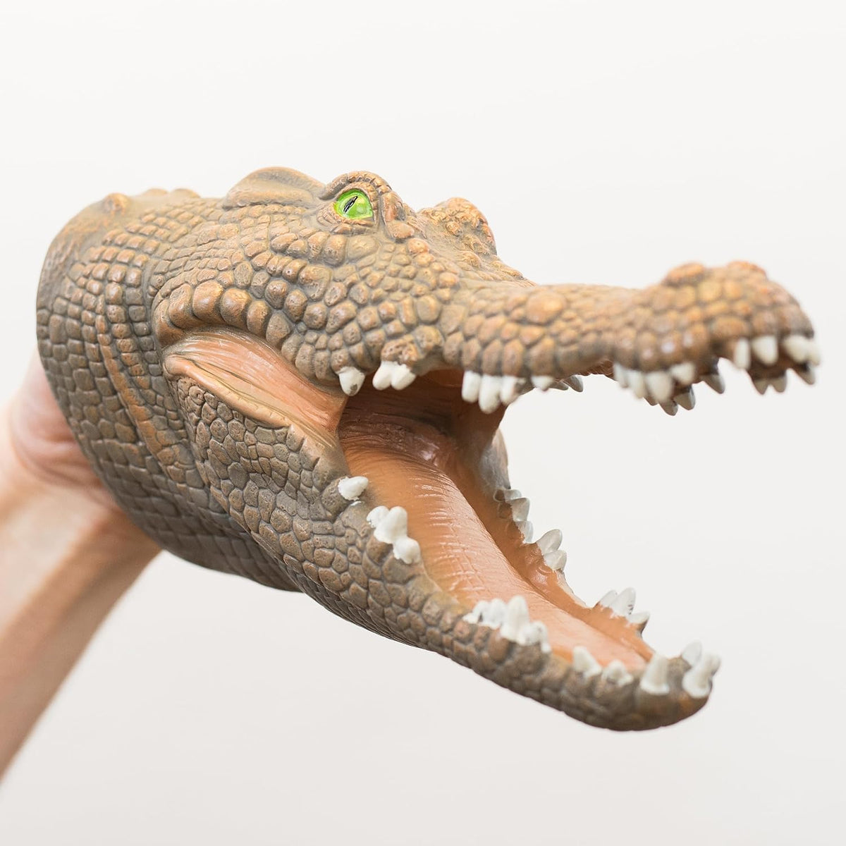 A realistic crocodile toy head with an open mouth, held by a hand against a plain light background.