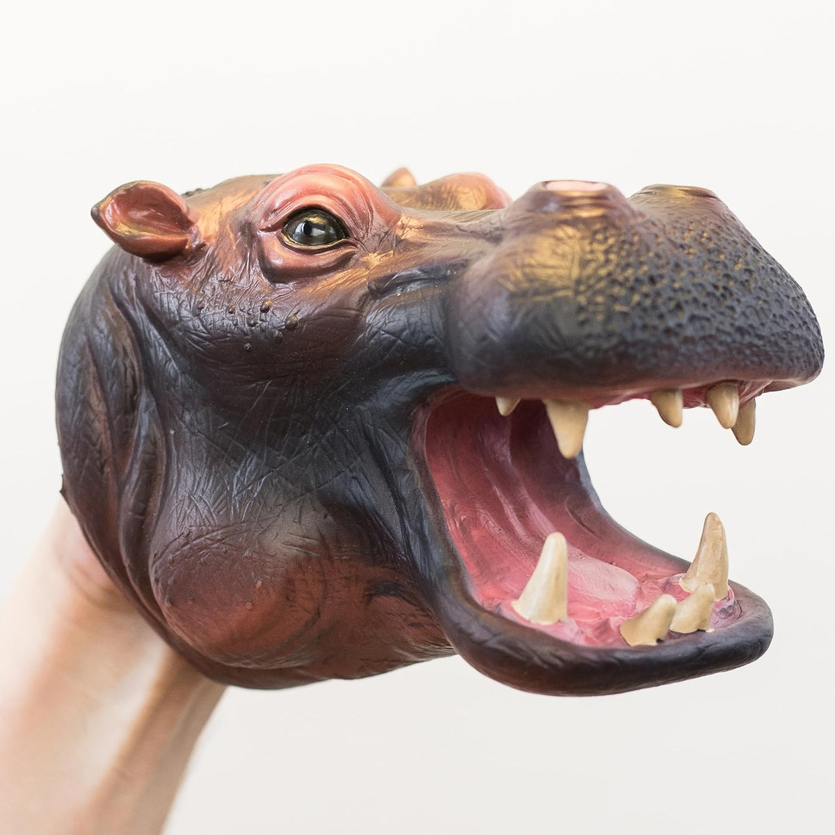 A realistic hippopotamus hand puppet being worn on a person's hand, with the mouth wide open showing sharp teeth and a pink interior, against a plain light background.
