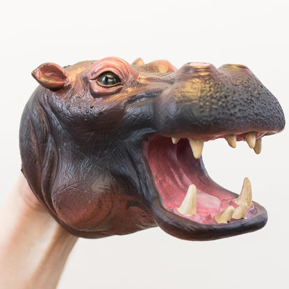 A realistic hippopotamus hand puppet being worn on a person's hand, with the mouth wide open showing sharp teeth and a pink interior, against a plain light background.
