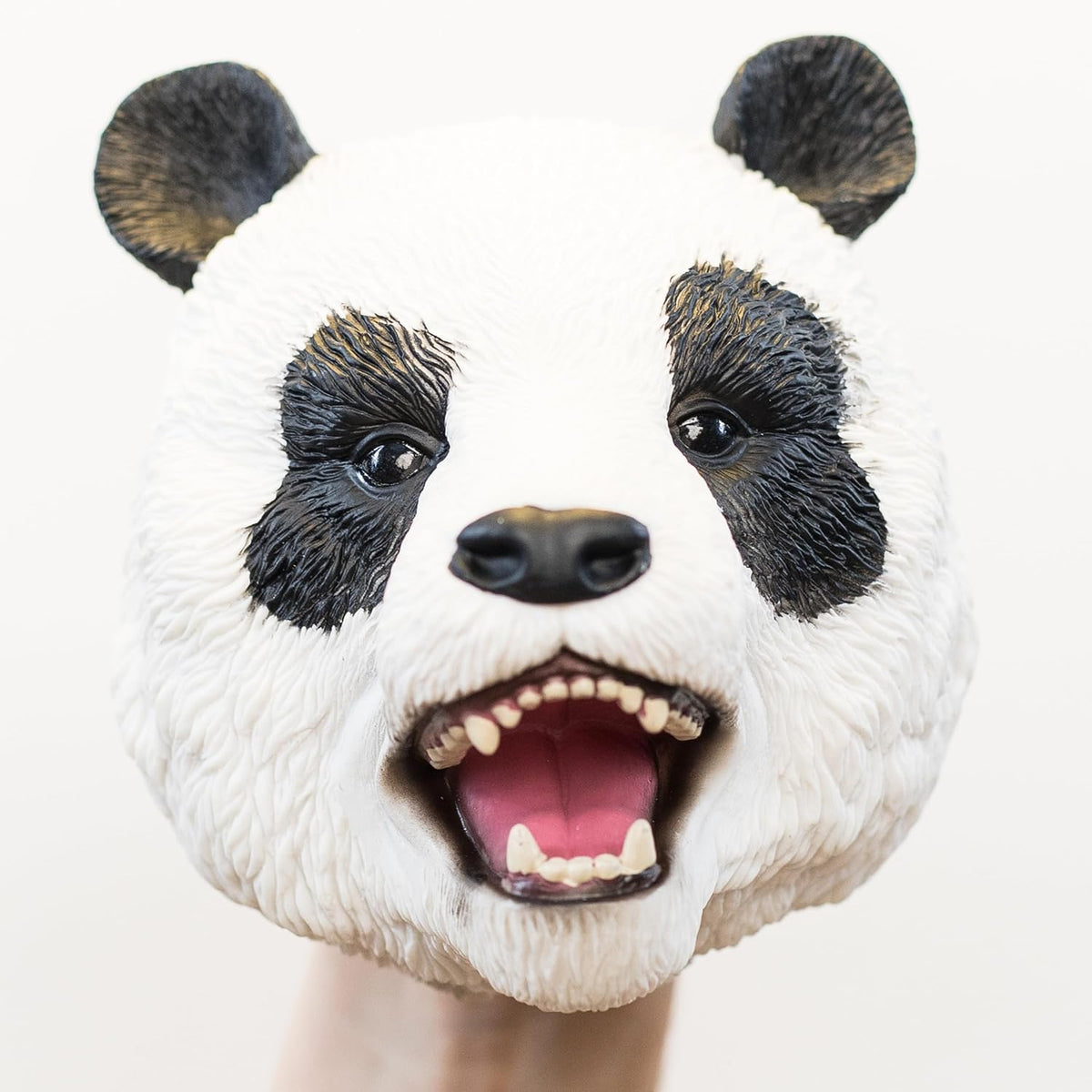 A realistic panda puppet with an open mouth showing teeth and a pink tongue, photographed against a plain light background.