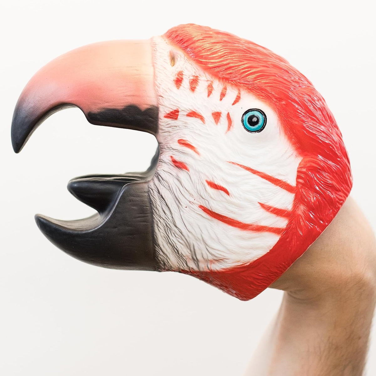 A close-up of a realistic red and white parrot puppet, showing the side profile with an open beak, blue eye, and textured feather details against a plain white background.