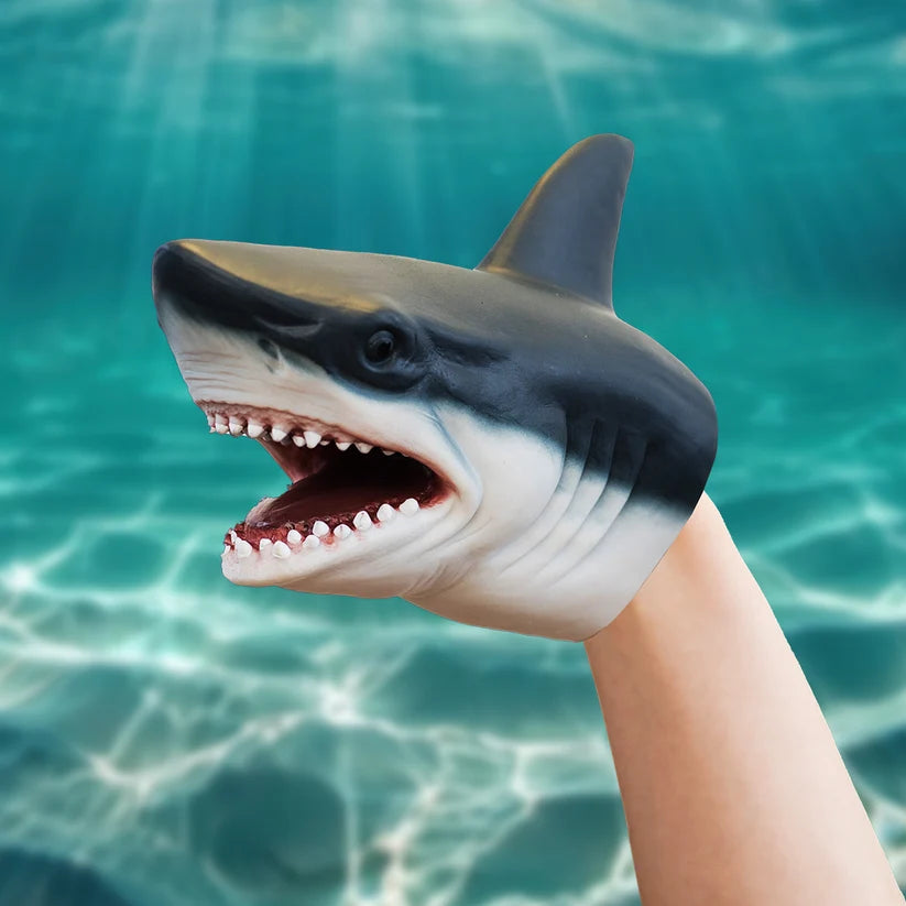 A shark-shaped hand puppet worn on a person's hand, with an open mouth showing teeth, set against a turquoise underwater pool background.