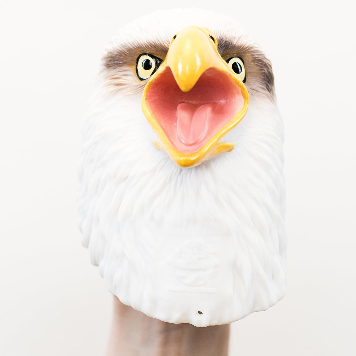 A close-up of a bald eagle head puppet with a white feathered face, brown eye patches, yellow beak, and open pink mouth, shown against a plain light background.