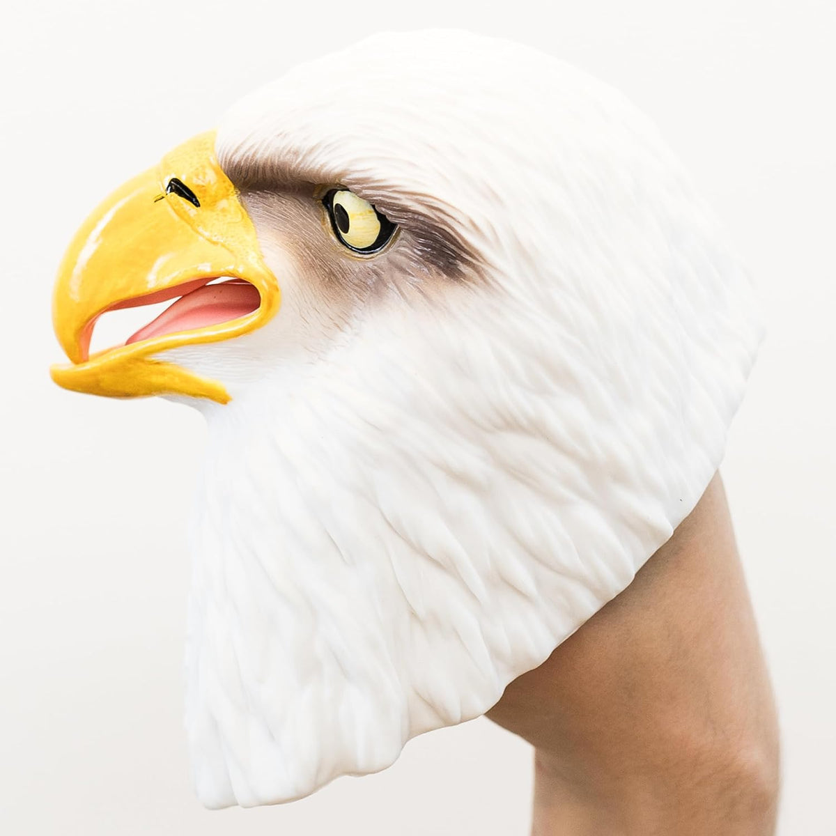 A realistic bald eagle head puppet shown on a person's hand against a plain light background.
